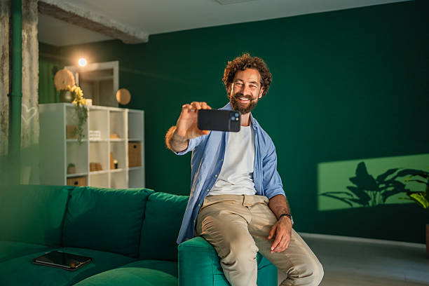 istock Smiling man taking self portrait while sitting on sofa in modern apartment 2231135449