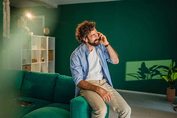 istock Smiling man talking on phone while sitting on sofa at home 2231135470