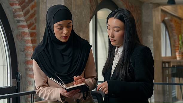 istock Serious concentrated two business women discussing startup project writing notes in notebook organizer planning job strategy multiracial females businesswomen girls Asian Muslim colleagues in office 2231137674