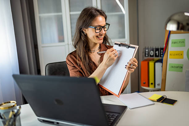 istock Young Woman on Video Call Showing Notes While Working from Home 2231145090
