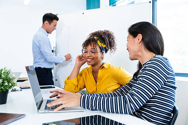 istock Businesswomen using laptop while businessman writing on whiteboard in office 2231148380