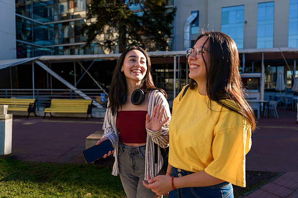 Two young latin american female students are walking and talking together on a university campus