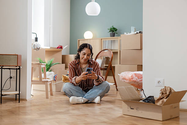 istock Woman unpacking boxes and using phone in her new home 2231151225
