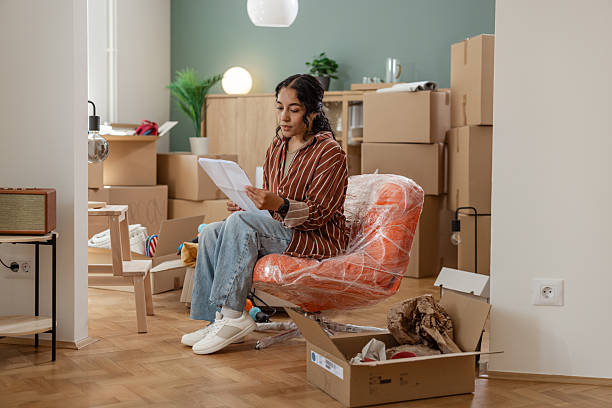 istock Young woman unpacking boxes while reading documents in her new apartment 2231151235