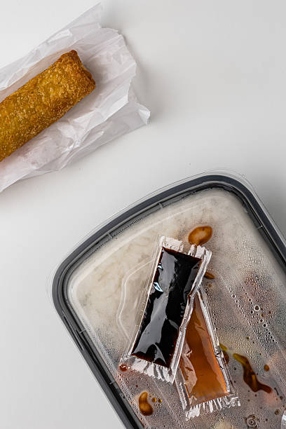 istock Asian cuisine to-go box with sauce packets and fried egg roll appetizer on white backdrop 2231155631