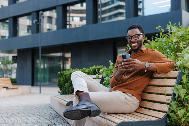 istock Smiling young man enjoying outdoor time while using smartphone on a bench 2231170315