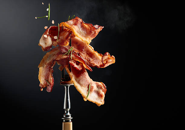 istock Fried bacon on a fork, sprinkled with rosemary and pink salt. 2231174722