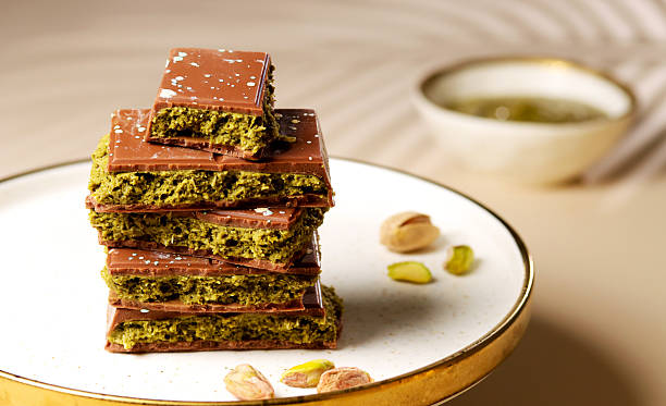 istock Dubai chocolate. Chocolate bars stacked elegantly on a plate, showcasing rich textures and vibrant colors, surrounded by pistachios and a bowl of green syrup, evoking indulgence and gourmet delight 2231183122