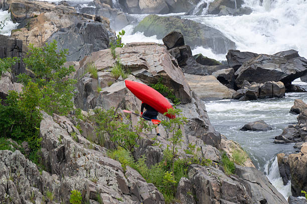Kayaker carrying his red kayak over the rocks with paddle in hand at Great Falls National Park