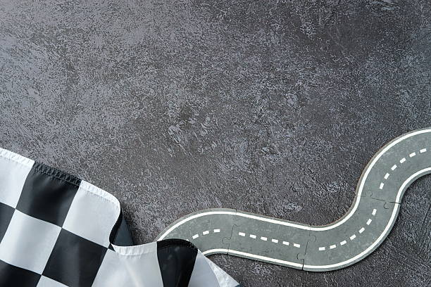 Winding puzzle road with dashed lines and checkered flag on dark textured background. Symbol of racing, finish line, and journey.
