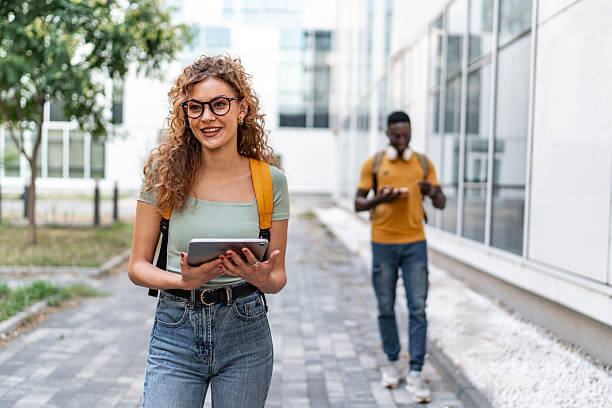 istock Smiling university student walking and using digital tablet outdoors 2231185246