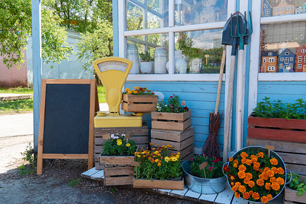 A charming rustic outdoor flower shop display with various potted flowers, wooden crates, and a large vintage yellow scale