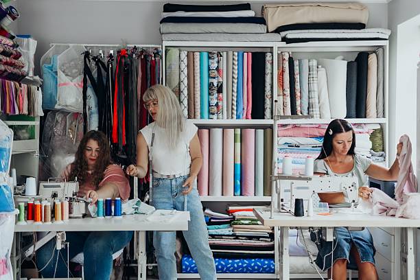 istock Three women working in colorful textile studio sewing fabrics on machines shelves full of folded materials teamwork female artisanship creative fashion workspace with vibrant threads and modern tools 2231193174