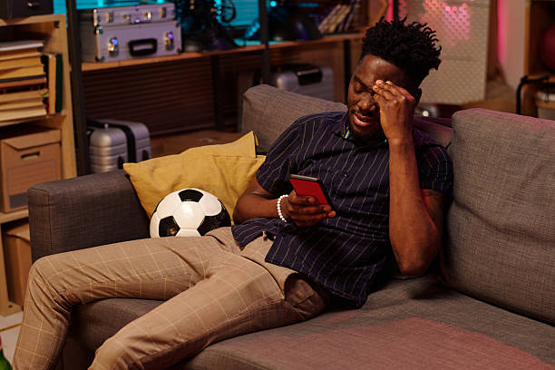 istock Young Adult Black Man Sitting on Sofa Checking Smartphone Looking Stressed 2231193668