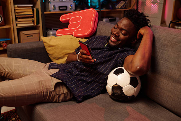 istock Young Adult Black Man Relaxing on Sofa Using Smartphone and Smiling 2231193706