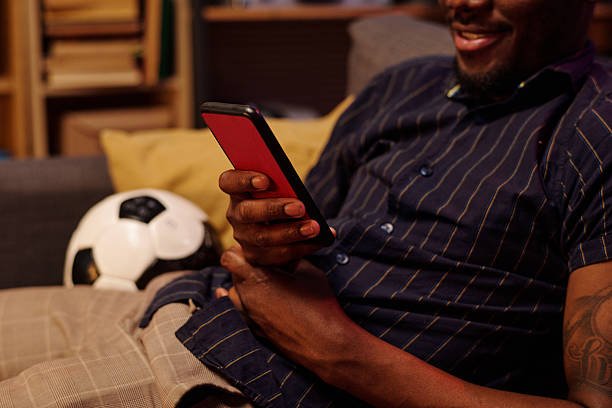 istock Young Adult Black Man Smiling While Browsing Smartphone Sitting with Soccer Ball 2231198218