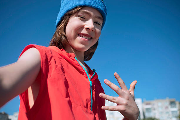 Selfie portrait of a smiling boy outdoors, showing playful hip hop hand signs, representing the joyful side of street culture and active youth lifestyle.
