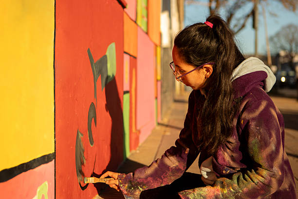 istock Young non-binary artist painting its artwork on a mural 2231215398