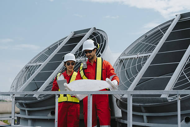 istock Industrial engineers working as a team, maintaining pipes, valves, air conditioning, refrigeration, HVAC systems at construction site. Male technicians in red safety uniforms checking pipe valves. 2231225208