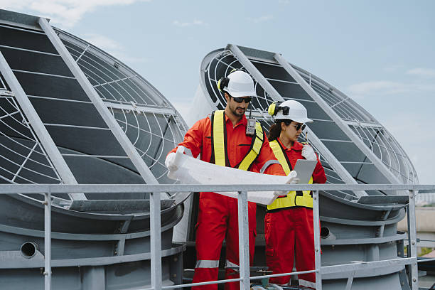 istock Industrial engineers working as a team, maintaining pipes, valves, air conditioning, refrigeration, HVAC systems at construction site. Male technicians in red safety uniforms checking pipe valves. 2231225228