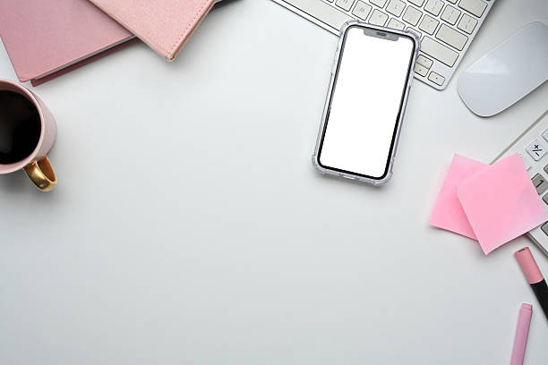 Minimal feminine workspace with smartphone, pink notebooks, sticky notes, and coffee cup on white desk.