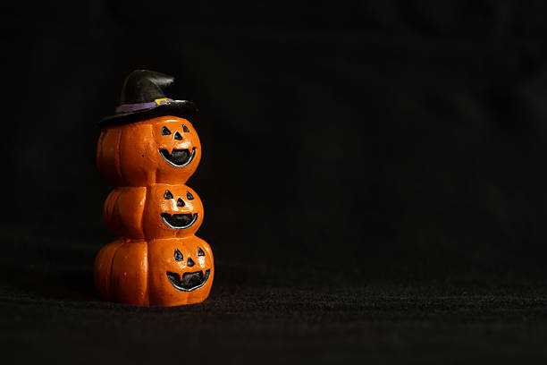 Stacked pumpkins with witch hat on dark background, Halloween holiday decoration concept.