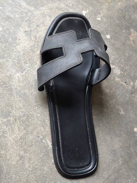 Single Black Slide Sandal Displayed on the Textured Grey Concrete Floor.