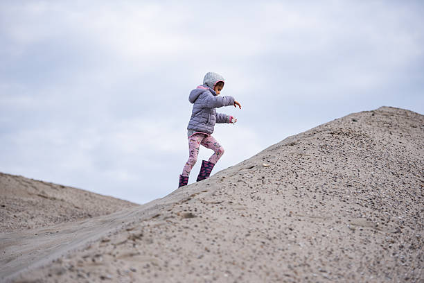 Child carefully climbing a steep sand dune, embracing the thrill of outdoor adventure on a cloudy, overcast day filled with exploration