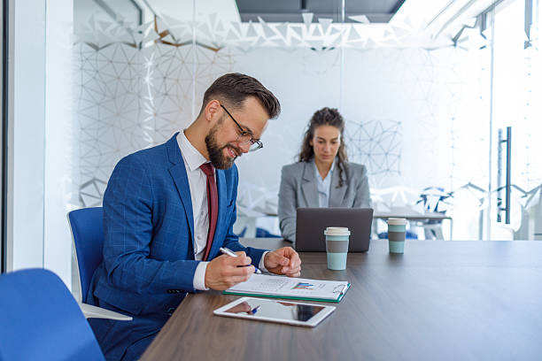 istock Businessman analyzing charts and taking notes in modern office with colleague 2231243199