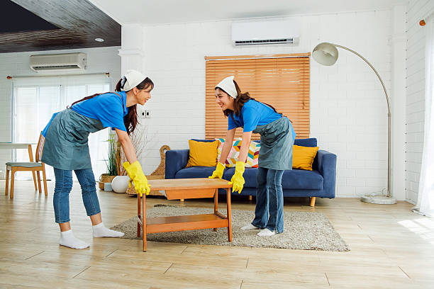 istock Two uniformed cleaners wearing gloves move a coffee table while tidying a bright modern living room with a blue sofa and wooden floor, illustrating professional housekeeping service. 2231245091