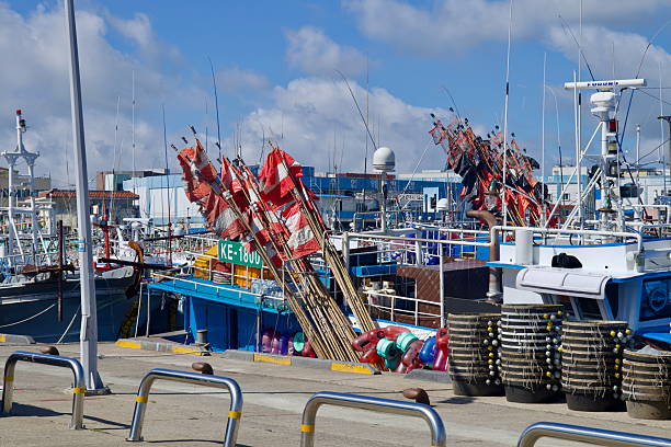 Stacks of fishing gear and bundles of red signal flags lean from trawlers at Hanlim Port on Jeju Island, surrounded by buoys, reels and masts in the crowded harbor.