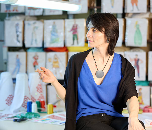 Attractive middle age woman fashion designer is working in her workshop. Shooting at the workplace