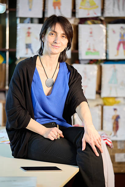 istock Cute female fashion designer sitting on the table while working in her studio, smiling looking on a side 2231261303
