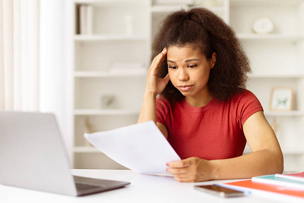 istock Young black woman looking stressed while reading documents at desk with laptop 2231262703