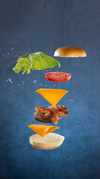 istock Floating hamburger composition with bun, beef patty, bacon, cheese, lettuce, and tomato on blue background 2231262835