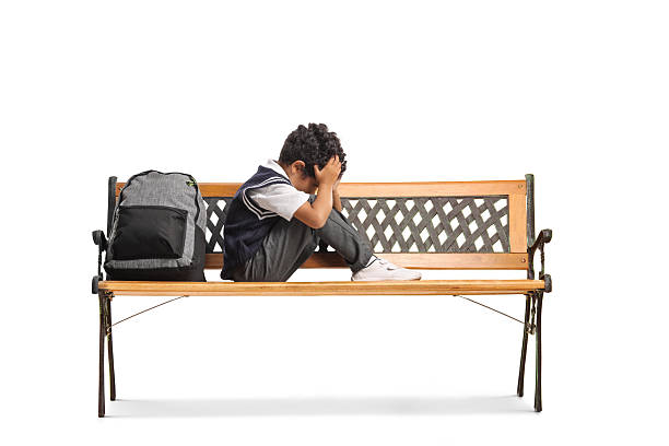 Sad lonely little schoolbot sitting on a bench isolated on white background