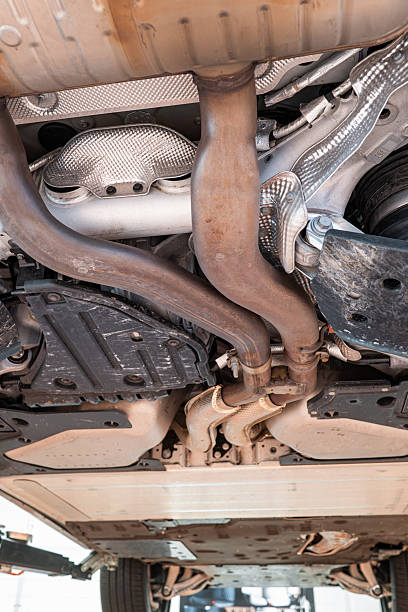istock Car undercarriage with exhaust system, wheels and axel components. Wide angle, looking up view, car suspended on a lift, inside repair shop, no people 2231273055
