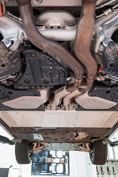 istock Car undercarriage with exhaust system, wheels and axel components. Wide angle, looking up view, car suspended on a lift, inside repair shop, no people 2231273070