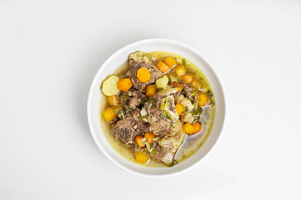 Delicious Indonesian beef rib soup with carrots, potatoes, and herbs in clear broth, served in a white bowl. Traditional homemade comfort food.