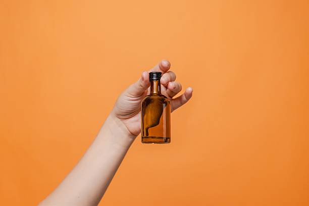 istock Elegant hand holding small glass blank bottle mockup on orange background. Package for cosmetics product, nutritional supplements, mixture, alcohol. Space for text 2231278929
