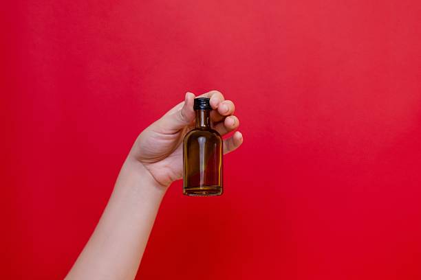 istock Elegant hand with small glass blank bottle mockup on red background. Package for cosmetics product, nutritional supplements, mixture, alcohol. Space for text 2231278932
