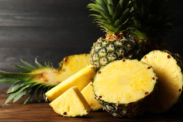 istock Whole and cut ripe pineapples on wooden table, closeup 2231281909