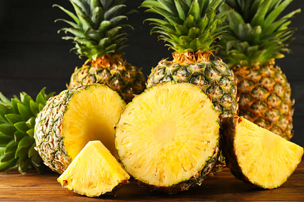 istock Whole and cut ripe pineapples on wooden table 2231281937