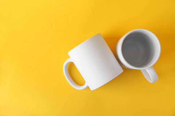 istock Two blank white mugs on yellow background, top view. Mockup for design 2231282401