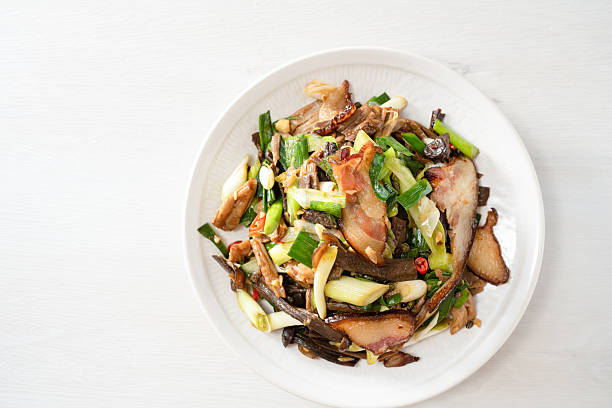 A top-down shot of a plate of alpine deer antler mushrooms and bacon on a white background