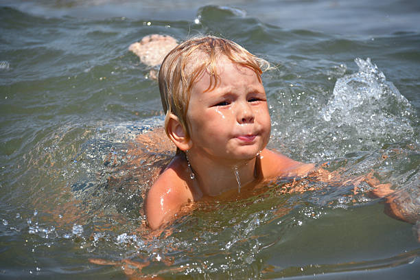 Happy boy run from the shore into the water. Summer childrens vacation on shore of lake or river. kid jump into water, swim and splash around at sunset. Active holidays. Dynamic image. Selective focus