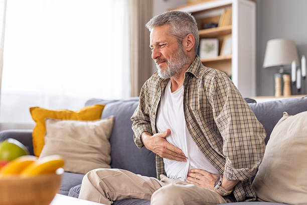 istock Man holding his stomach in pain while resting on the couch. 2231297602