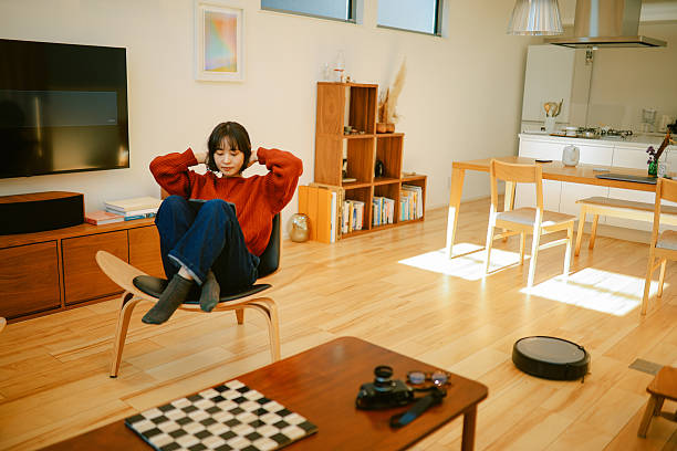 Woman is relaxing, reading or studying on her digital tablet while the robot vacuum cleaner is operating at home. Smart home concepts in Tokyo, Japan.