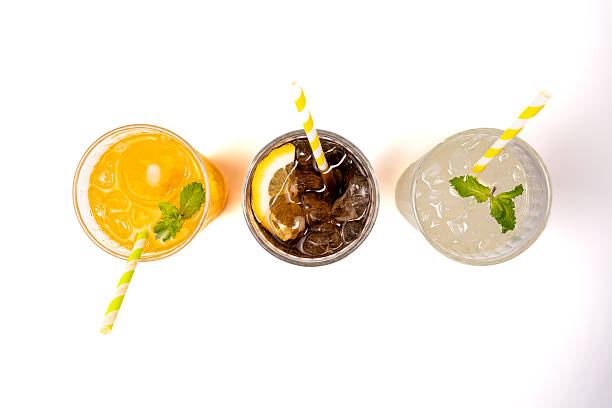 Chilled beverages garnished with mint, served in glasses with ice and colorful straws, viewed from overhead white setting