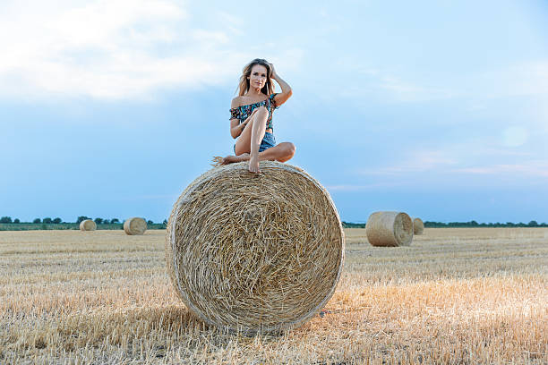 istock Young woman sitting on a round haystack in a mowed wheat field 2231308999